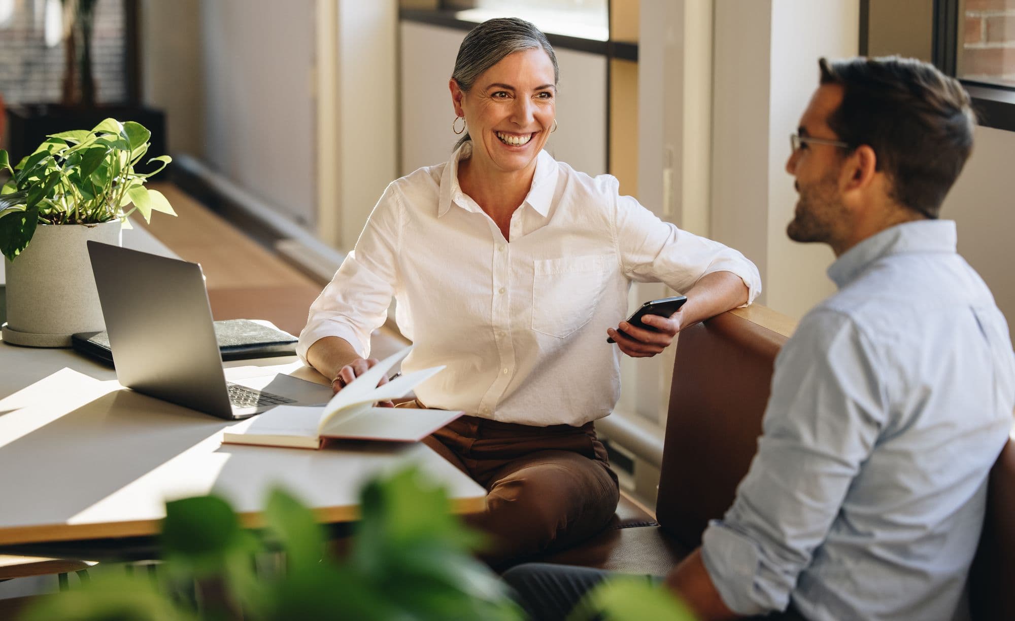 Two colleagues talk and laugh across a desk