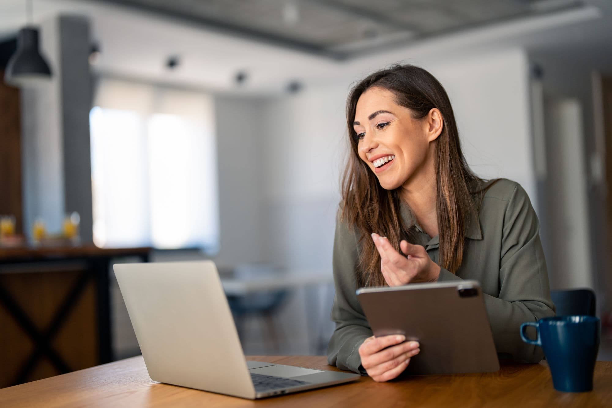 A woman laughs as she works between her laptop and a tablet
