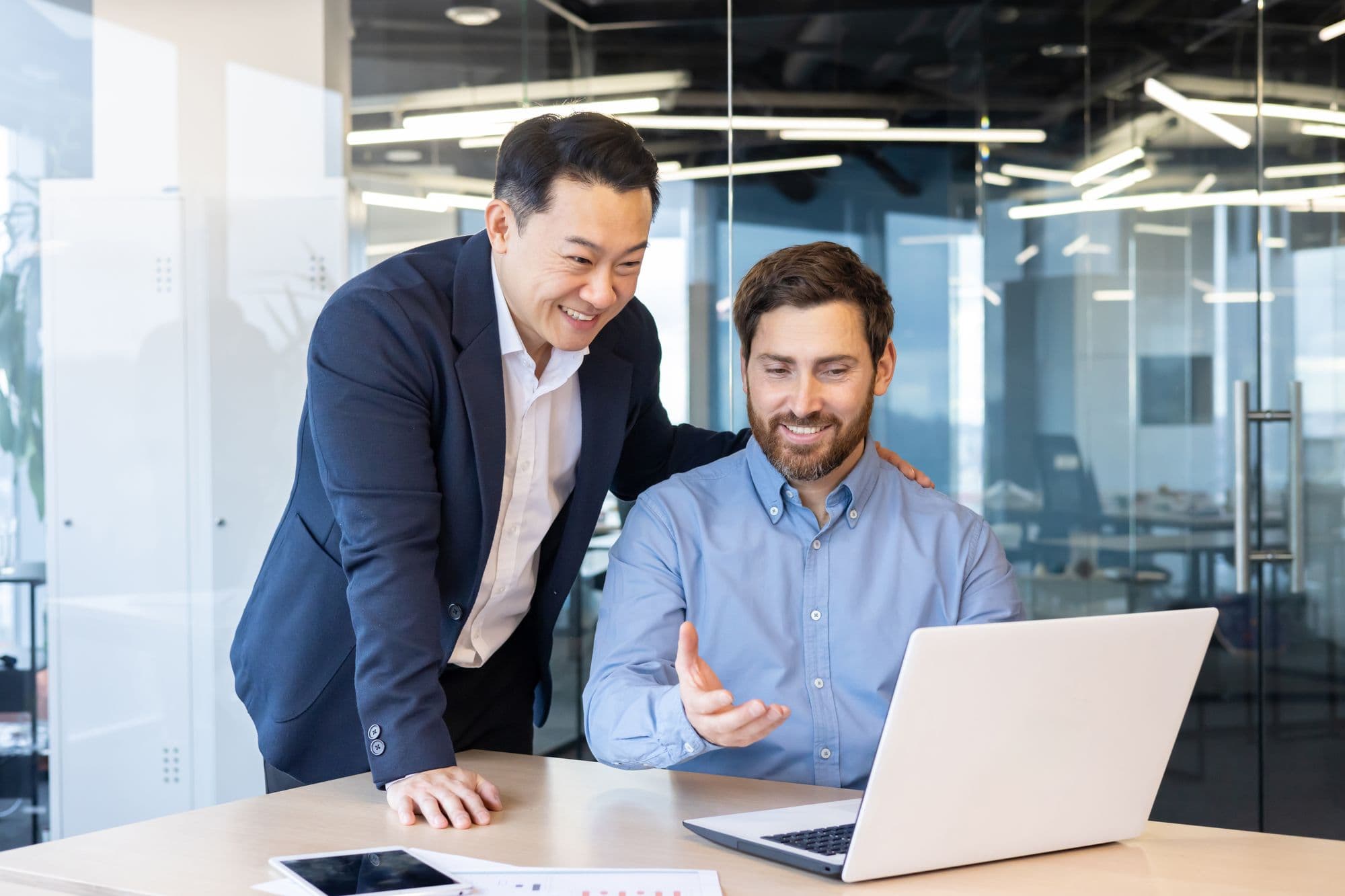 A senior manager guides a newer colleague at a laptop