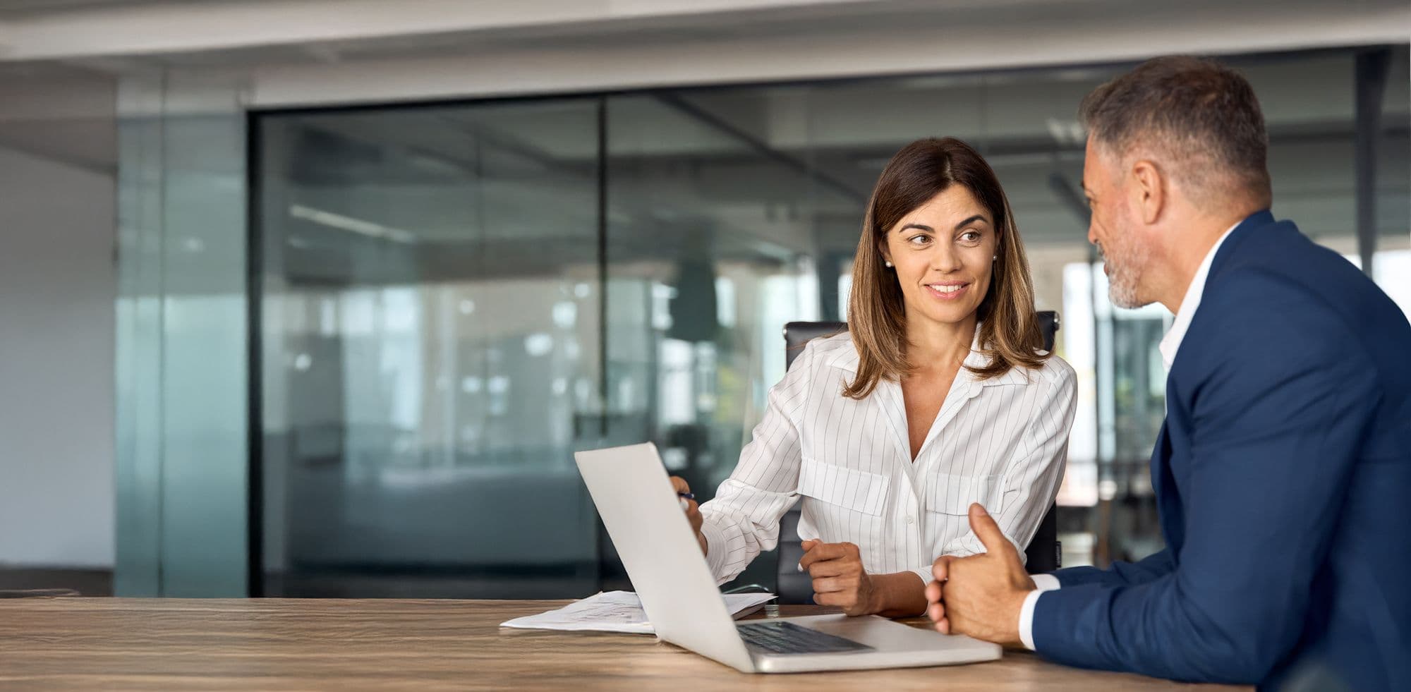 An experienced leader talks with a younger colleague over a laptop in a meeting room