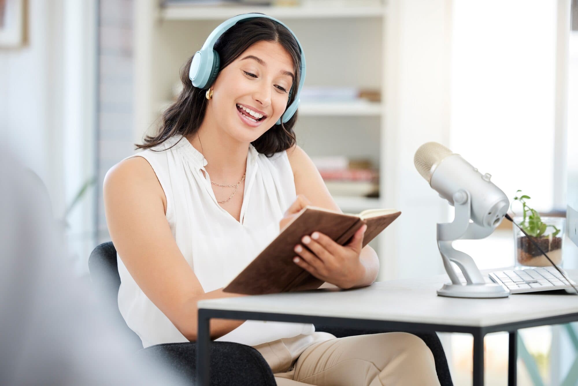 A woman with headphones writes notes at a podcast microphone