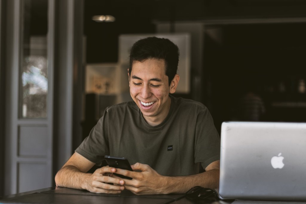 man laughing at phone outside cafe during virtual mentoring session