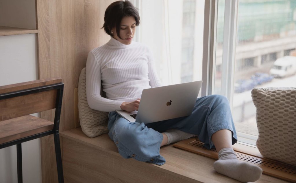 woman using laptop sitting in window