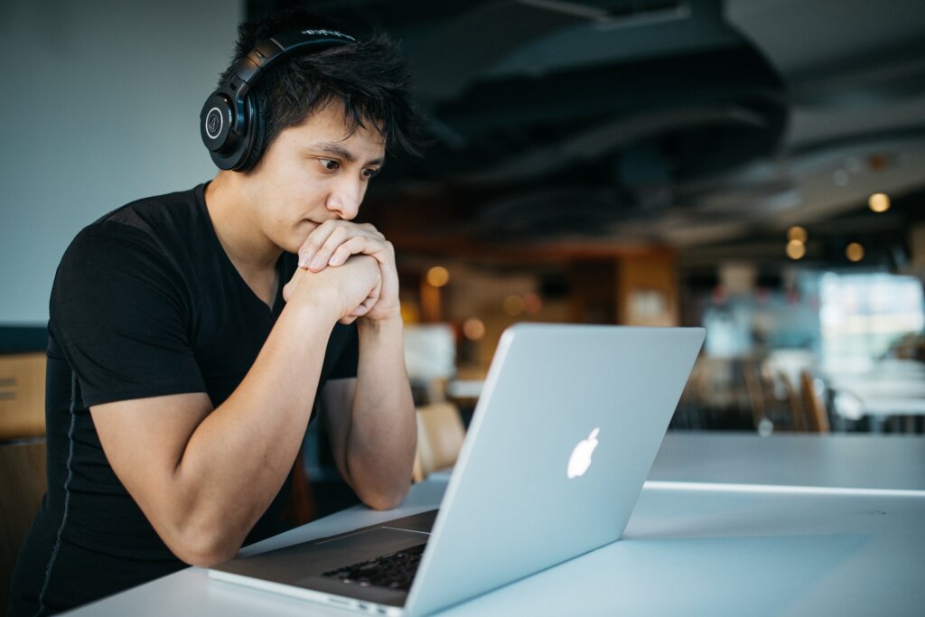asian male employee with headphones on staring at laptop concerned