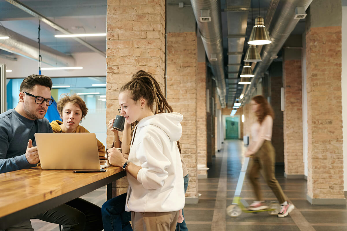 employees standing around a laptop in a modern office discussing mentoring program ideas