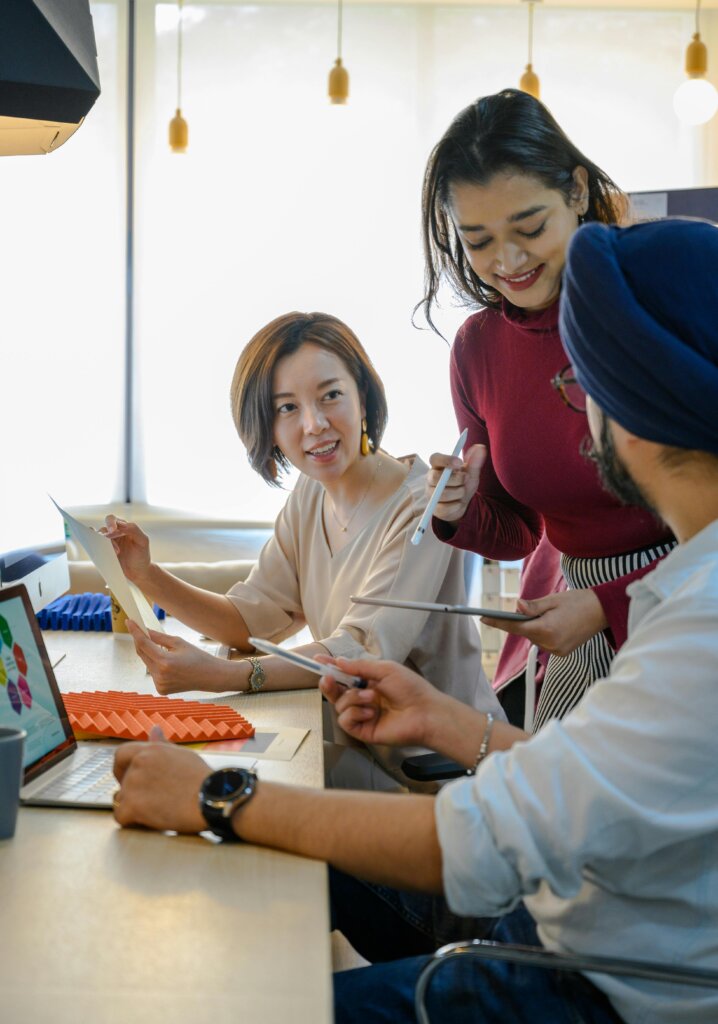 two women employees working with a male employee at desk, looking at documents and reports