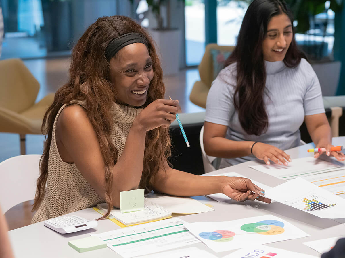 two women employees smiling and looking over DEIB reports at a desk in the office