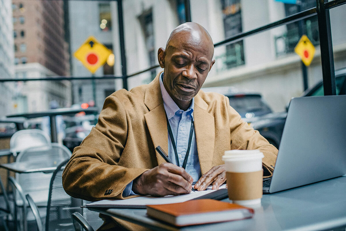 black male employee sitting at cafe writing notes on a pad about the stat of DEIB in his company