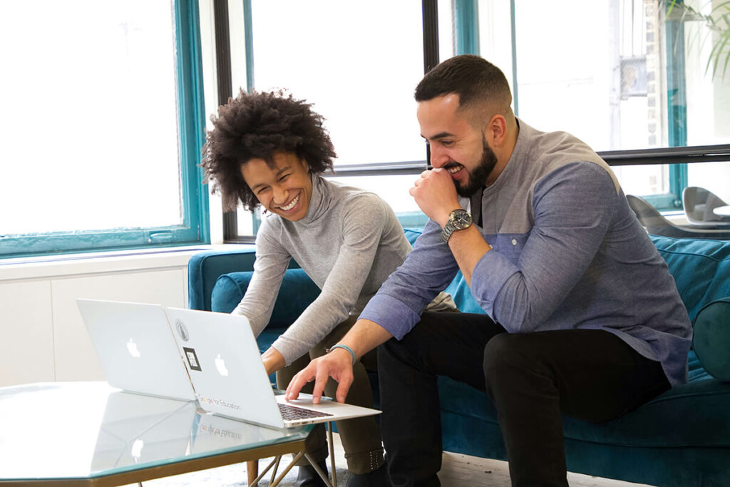 female employee and male employee sit on couch and work on laptops determining mentoring program ideas for the next quarter