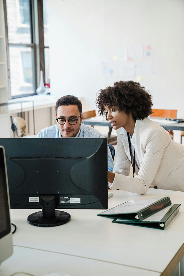 peer mentoring session in action with male employee and woman employee working on a desktop computer in an office