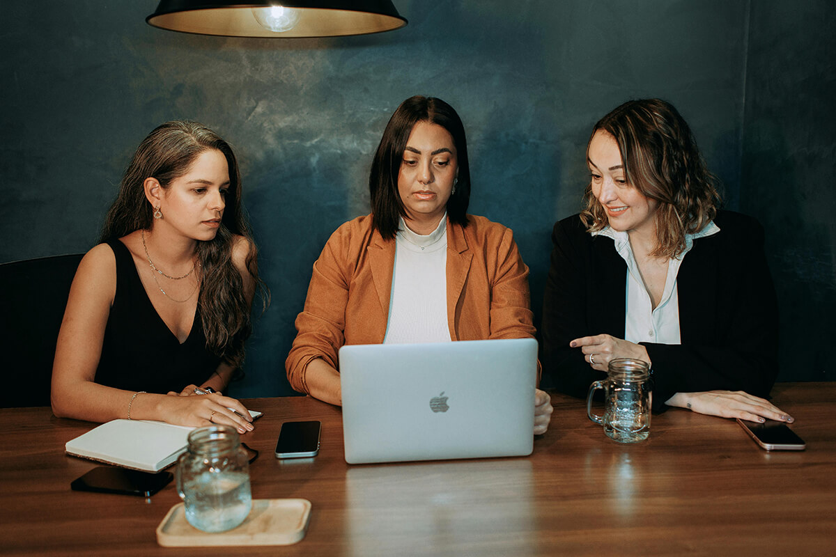 three women employees sitting at table talking about peer mentoring best practices