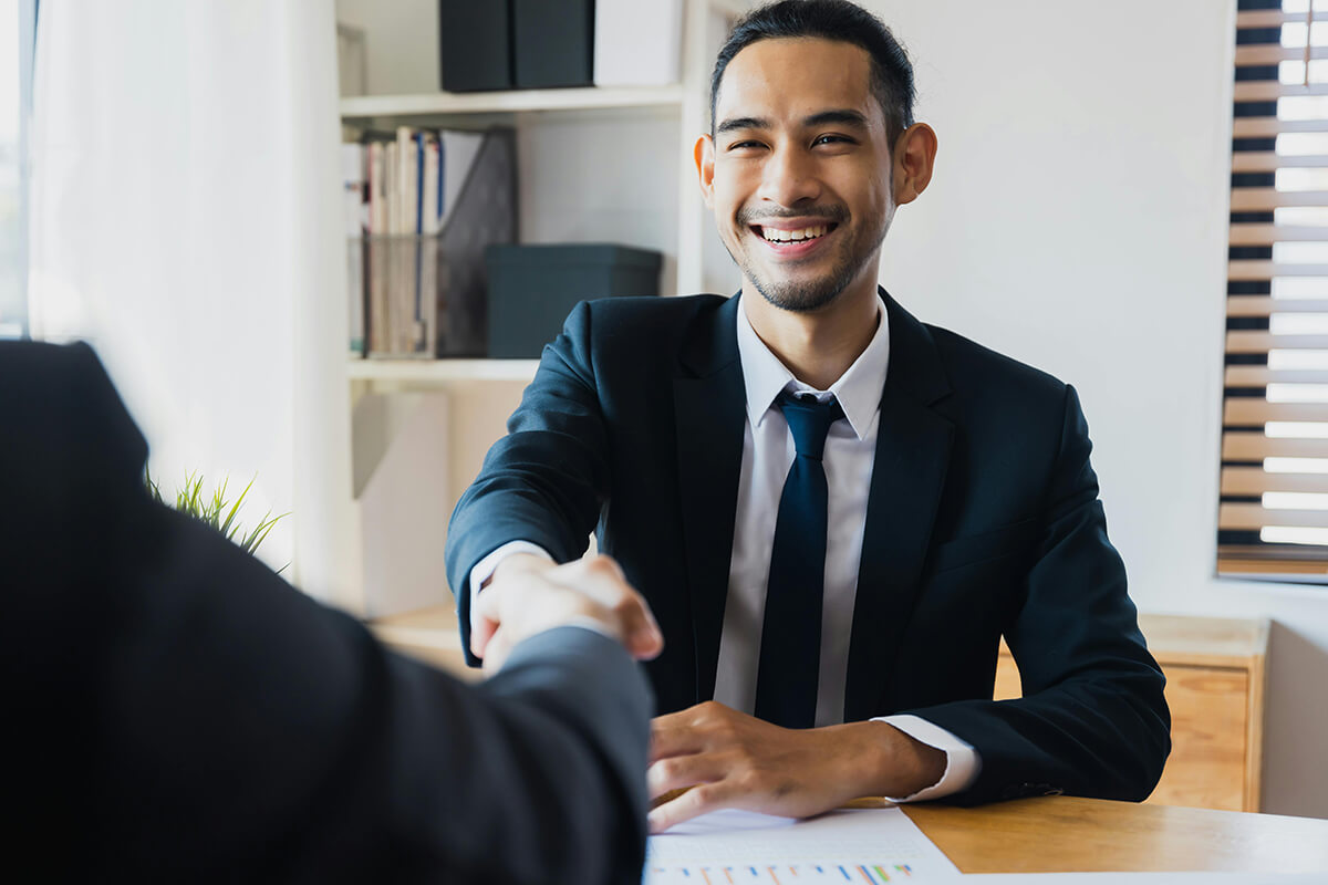 man sitting in an office at a desk shaking hands with another colleague after aligning on his talent development strategy