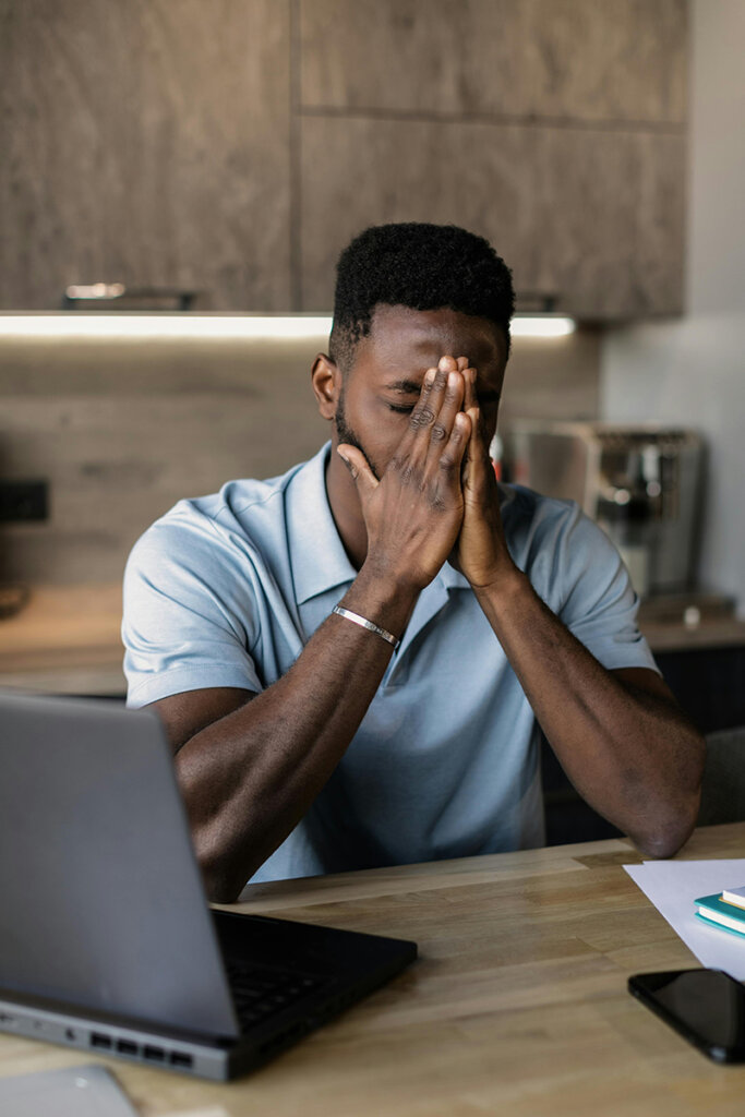 Black male employee experiencing frustration trying to break through organizational silos. Sitting at a counter in the office with laptop open.