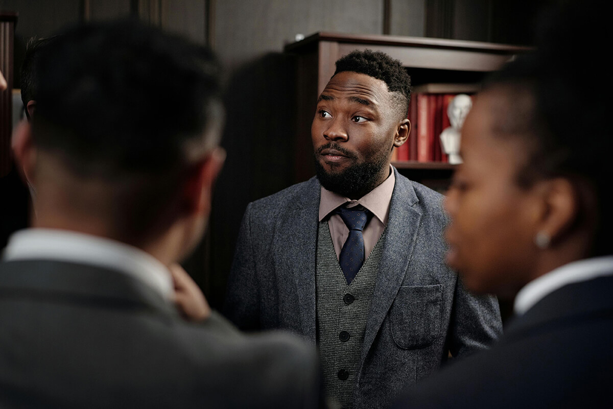 Black male employee standing in a suit participating in a conversation about the organization's mentoring culture