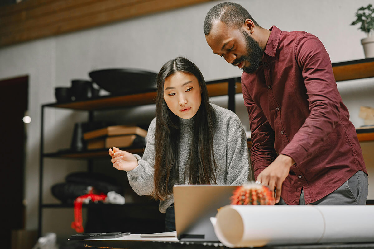 man and woman standing at a desk in an office looking at a laptop as they discuss collaborative culture at their company