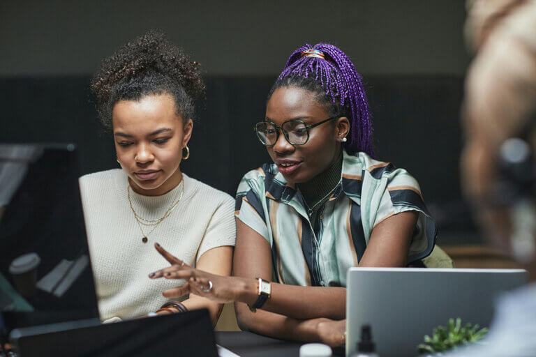 Two women sitting in an office looking at a desktop computer as part of a team mentoring session