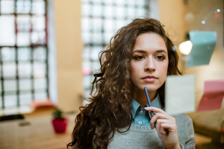 Woman standing in a conference room looking at post-it notes on the wall, pondering her next professional goals