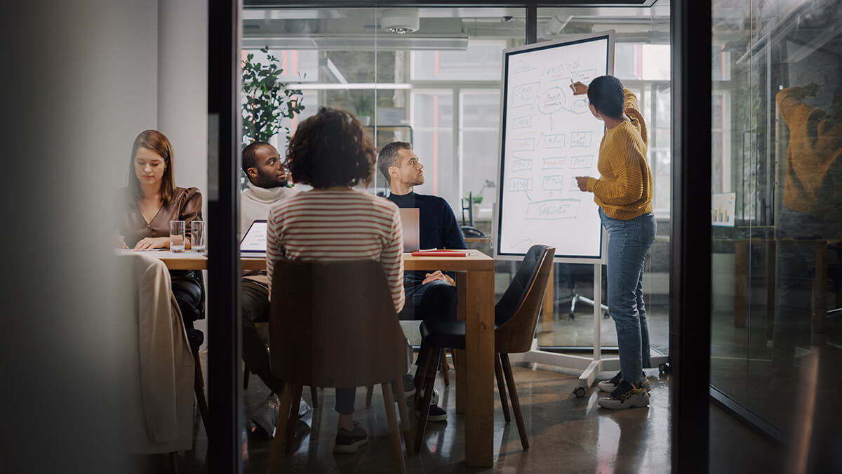 Woman leading a meeting at a whiteboard in a conference room of teammates, discussing professional goals for the company and employees