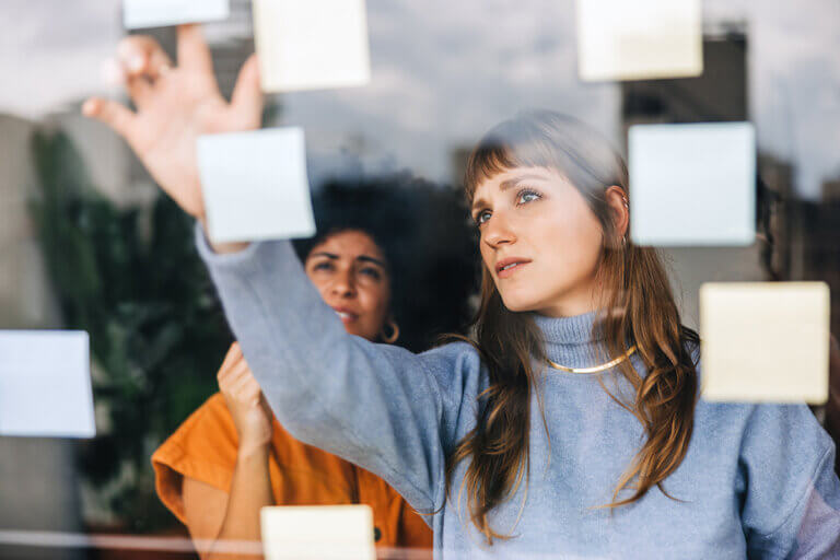 Two women standing at a window putting post-it notes up during a growth mindset brainstorm