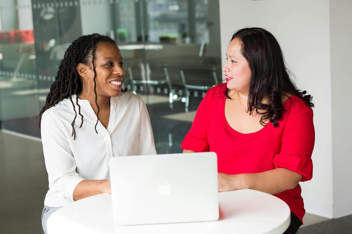 Two colleagues meet at a small company cafe table with a laptop between them