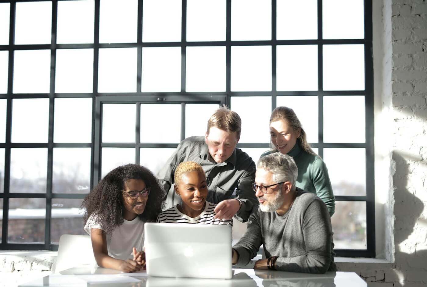 Coworkers look at a laptop together in a conference room.