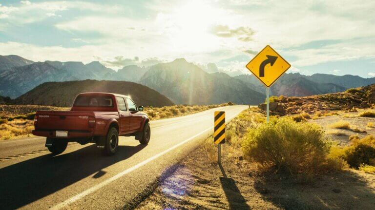 Red pickup truck driving past a sign indicating a curve ahead