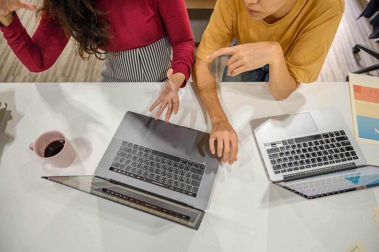 A pair of professionals discuss what they're seeing on a laptop screen.