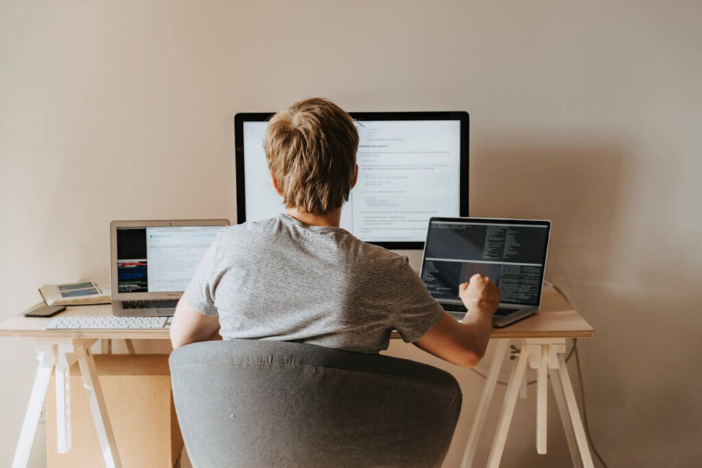 A professional works at a clean, modern desk with two laptops and a large monitor.